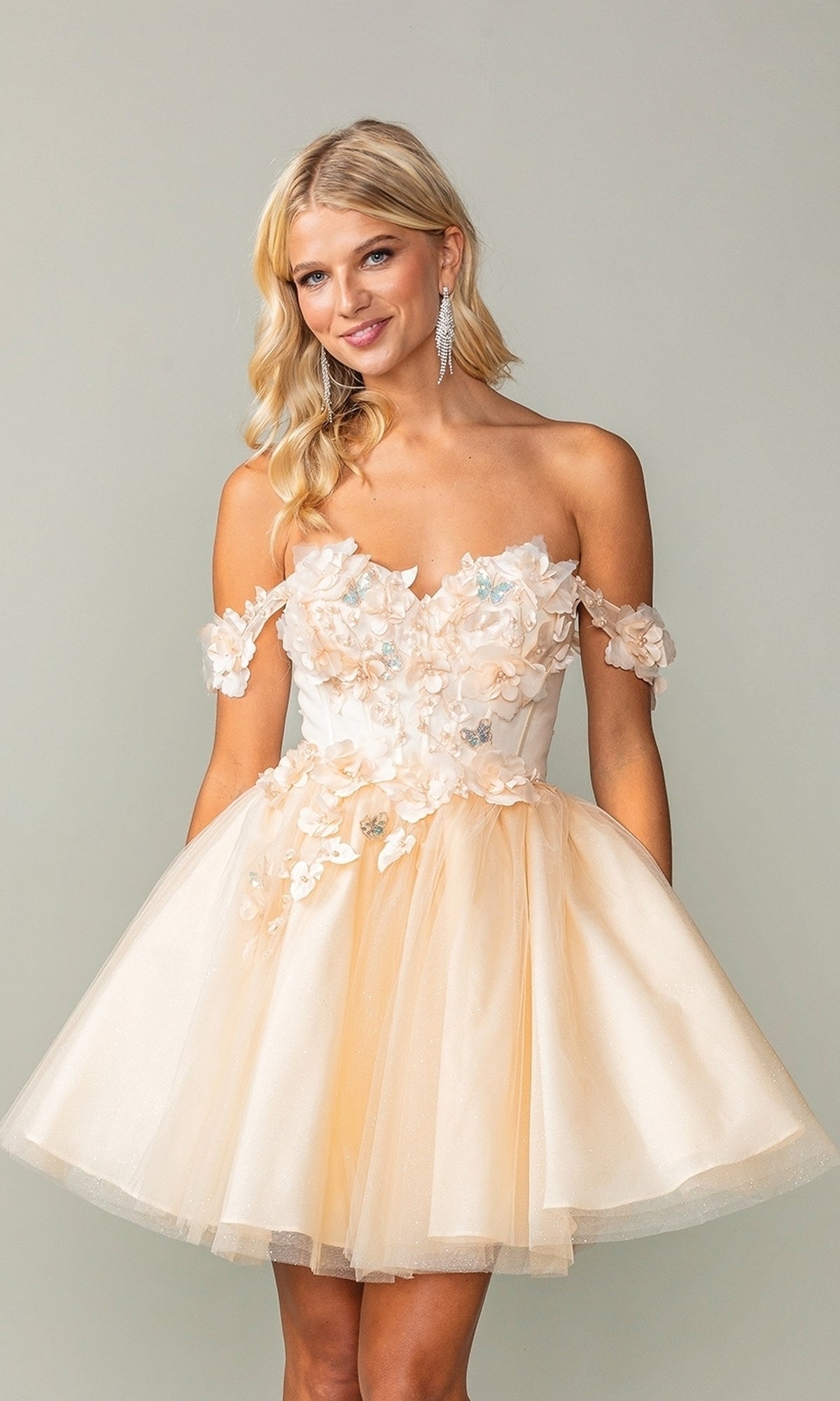 A woman models the Off-Shoulder Short Babydoll Homecoming Dress 3388, featuring floral appliqués and a tulle skirt, against a plain light background.